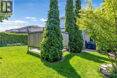 Expansive green lawn featuring a privacy fence, mature trees, and a paved patio area - 640 Acadia Drive, Hamilton, ON 