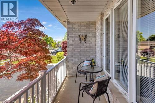 Covered balcony featuring light-toned brickwork, durable railing, and a vibrant red-leaf tree - 640 Acadia Drive, Hamilton, ON 