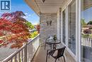 Covered balcony featuring light-toned brickwork, durable railing, and a vibrant red-leaf tree - 640 Acadia Drive, Hamilton, ON 