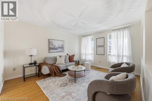 Bright living space featuring warm wood-finish flooring, light-toned walls, and large windows with white sheer curtains - 957 Stone Church Road E, Hamilton, ON - Indoor Photo Showing Living Room