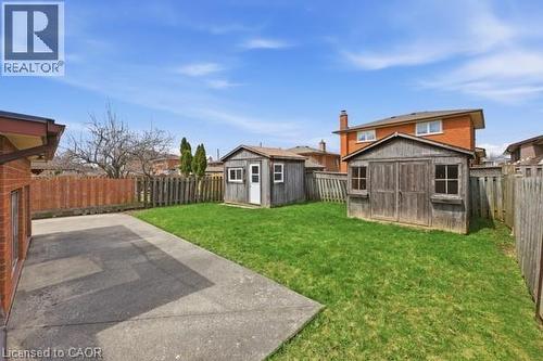 Expansive rear yard featuring a concrete patio, manicured lawn, and two detached storage sheds - 957 Stone Church Road E, Hamilton, ON - Outdoor