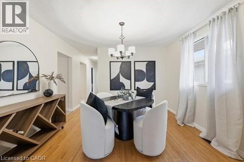 Dining area featuring hardwood flooring, a multi-light chandelier, a large window with white curtains, and a built-in wood-finish console with storage - 957 Stone Church Road E, Hamilton, ON - Indoor