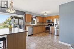 Kitchen featuring wood-finish cabinetry, stainless steel appliances, tiled flooring, and a sliding glass door to an exterior covered patio - 