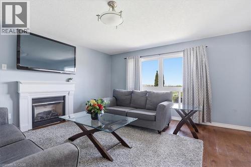 Living area featuring a fireplace with a white mantel, a large window with patterned drapes, a ceiling-mounted light fixture, and wood-finish flooring - 136 Carpenter Road, Cambridge, ON - Indoor Photo Showing Living Room With Fireplace