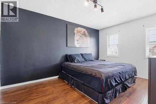 Bedroom featuring two windows with horizontal blinds, wood-finish flooring, and a dark accent wall - 136 Carpenter Road, Cambridge, ON - Indoor Photo Showing Bedroom
