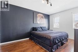 Bedroom featuring two windows with horizontal blinds, wood-finish flooring, and a dark accent wall - 