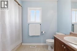 Bathroom with a window, white shower curtain, tiled flooring, wood-finish vanity with a countertop, and an oval sink - 