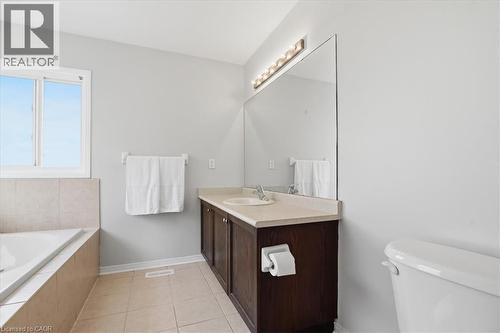 Bathroom featuring a built-in bathtub with tiled surround, a window, a dark wood-finish vanity with an integrated sink and light countertop, and a large wall-mounted mirror with overhead lighting - 136 Carpenter Road, Cambridge, ON - Indoor Photo Showing Bedroom