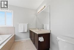 Bathroom featuring a built-in bathtub with tiled surround, a window, a dark wood-finish vanity with an integrated sink and light countertop, and a large wall-mounted mirror with overhead lighting - 