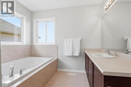 Bathroom featuring a built-in tub with tiled surround, dual windows, and a vanity with an integrated sink and wood-finish cabinetry - 136 Carpenter Road, Cambridge, ON - Indoor Photo Showing Bathroom
