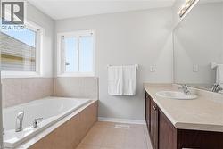 Bathroom featuring a built-in tub with tiled surround, dual windows, and a vanity with an integrated sink and wood-finish cabinetry - 
