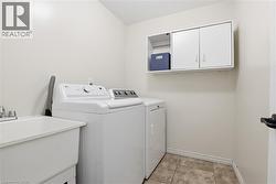 Dedicated laundry area featuring a utility sink with a two-handle faucet, wall-mounted cabinetry with an open shelf, and neutral-toned wall paint - 