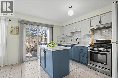 Kitchen featuring a central island with countertop, two-tone cabinetry, subway tile backsplash, stainless steel gas range, and a sliding glass door leading to an exterior deck - 236 Fitzgerald Crescent, Milton, ON - Indoor Photo Showing Kitchen