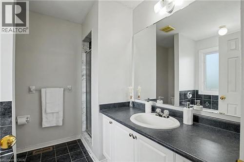 Full bathroom featuring a single vanity with a white basin sink, a dark countertop, white cabinetry, a large wall mirror, and a glass-enclosed shower with white and gray tiled walls - 236 Fitzgerald Crescent, Milton, ON - Indoor Photo Showing Bathroom