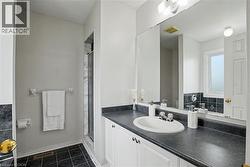 Full bathroom featuring a single vanity with a white basin sink, a dark countertop, white cabinetry, a large wall mirror, and a glass-enclosed shower with white and gray tiled walls - 