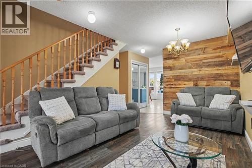 Living area featuring wood-finish flooring, a wood accent wall, and a chandelier - 236 Fitzgerald Crescent, Milton, ON - Indoor Photo Showing Living Room