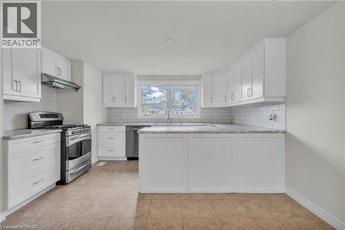 Open-concept kitchen featuring white cabinetry, subway tile backsplash, stainless steel appliances, granite countertops, and tile flooring - 22 Blackhorne Crescent, Kitchener, ON - Indoor Photo Showing Kitchen