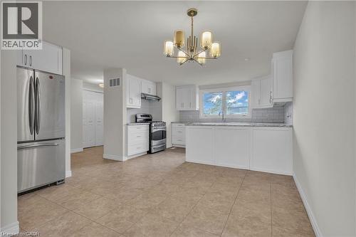 Bright kitchen featuring white cabinetry, stainless steel appliances, a modern chandelier, a white subway tile backsplash, and a window above the sink - 22 Blackhorne Crescent, Kitchener, ON - Indoor Photo Showing Kitchen