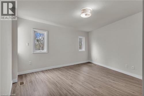 Spacious room featuring wood-finish flooring, two large windows, white baseboards, and a decorative ceiling light fixture - 22 Blackhorne Crescent, Kitchener, ON - Indoor Photo Showing Other Room