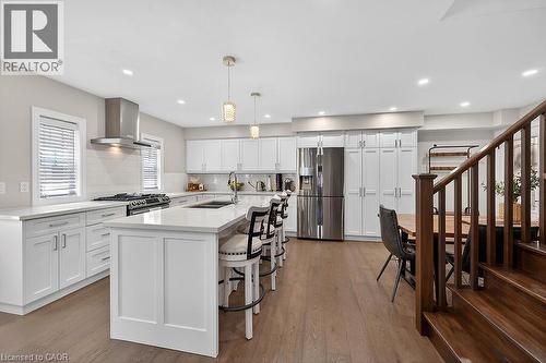 Open-concept kitchen featuring a large central island with seating, white shaker cabinetry, stainless steel appliances, and wood-finish flooring - 109 Ray Street N, Hamilton, ON - Indoor Photo Showing Kitchen With Upgraded Kitchen