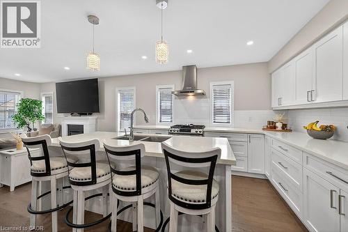 Modern kitchen featuring a central island with an undermount double sink and chrome faucet, white shaker cabinetry, light-toned countertops, a subway tile backsplash, and stainless steel appliances - 109 Ray Street N, Hamilton, ON - Indoor