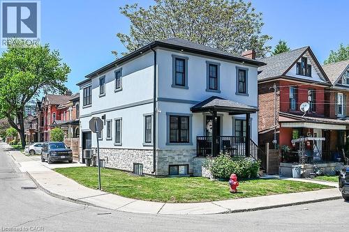 Two-story stucco exterior featuring stone veneer siding on the lower level, a covered front porch with dark railings, black-framed windows, and a corner lot location with a manicured lawn - 109 Ray Street N, Hamilton, ON - Outdoor With Facade