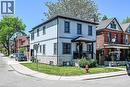Two-story stucco exterior featuring stone veneer siding on the lower level, a covered front porch with dark railings, black-framed windows, and a corner lot location with a manicured lawn - 109 Ray Street N, Hamilton, ON  - Outdoor With Facade 