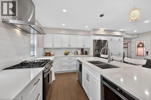 Modern kitchen featuring white shaker cabinetry, stainless steel appliances, a center island with a double basin sink, recessed lighting, and wood-finish flooring - 109 Ray Street N, Hamilton, ON - Indoor Photo Showing Kitchen With Double Sink With Upgraded Kitchen