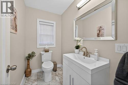 Powder room featuring a single vanity with an integrated sink, a rectangular mirror, a window with blinds, and tile flooring - 109 Ray Street N, Hamilton, ON - Indoor Photo Showing Bathroom