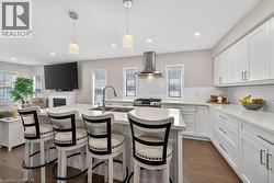Modern kitchen featuring a central island with an undermount double sink and chrome faucet, white shaker cabinetry, light-toned countertops, a subway tile backsplash, and stainless steel appliances - 