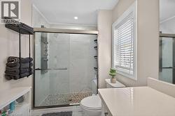Contemporary bathroom featuring a glass-enclosed shower with tile surround and pebble flooring, a white window with blinds, and a light-toned countertop - 