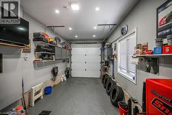 Attached garage featuring a white overhead door, multiple recessed lights, built-in shelving, a window with blinds, and a wall-mounted television - 