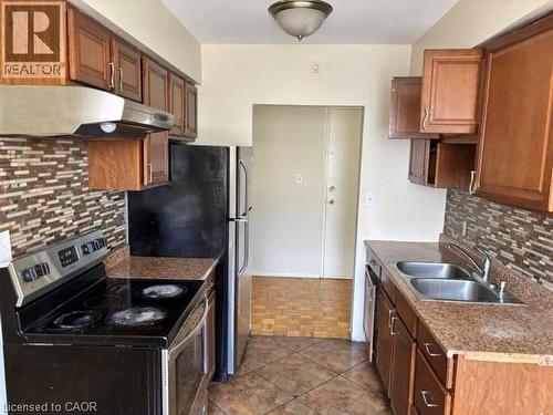 Kitchen featuring warm wood cabinetry, granite-style countertops, mosaic tile backsplash, and stainless steel sink - 2205 King Street E Unit# 1, Hamilton, ON - Indoor Photo Showing Kitchen With Double Sink