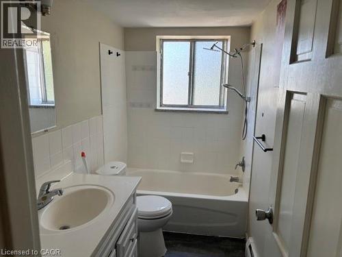 Bathroom featuring a full bathtub with tile surround, a single vanity with an integrated sink, a built-in medicine cabinet, and a window providing natural light - 2205 King Street E Unit# 1, Hamilton, ON - Indoor Photo Showing Bathroom
