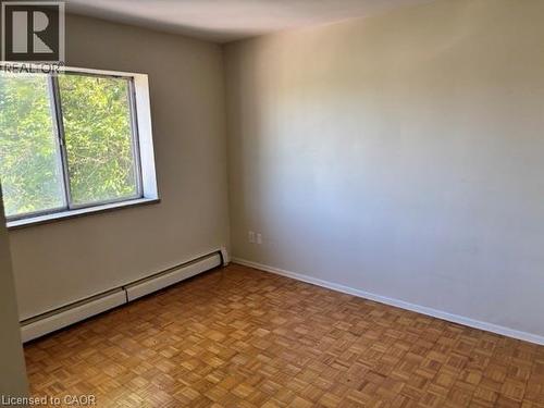 Room featuring a large window, parquet wood-finish flooring, light-toned walls, and baseboard heating - 2205 King Street E Unit# 1, Hamilton, ON - Indoor Photo Showing Other Room