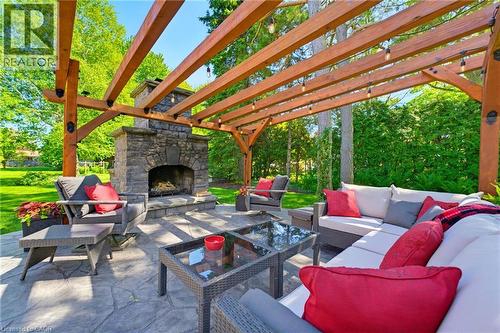 Outdoor living space featuring a wood pergola with integrated string lighting, a stone-clad fireplace, and a textured paver patio - 169 James Street, Atwood, ON - Outdoor With Deck Patio Veranda