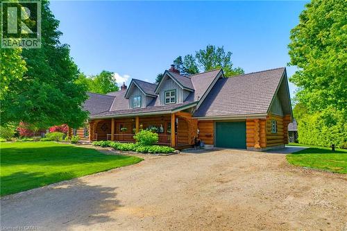 Log cabin style residence featuring a prominent covered front porch, an attached garage with a green door, multiple gabled rooflines, and dormer windows - 169 James Street, Atwood, ON - Outdoor With Deck Patio Veranda