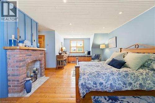 Spacious room featuring wood-finish flooring, a brick fireplace with a wood mantle, a window seat with storage, and a paneled ceiling with recessed lighting - 169 James Street, Atwood, ON - Indoor Photo Showing Bedroom With Fireplace