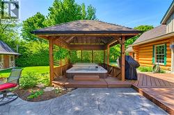 Covered outdoor spa area with a wood pergola, integrated hot tub, multi-level wood decking, and stamped concrete patio - 