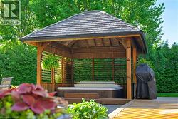 Expansive outdoor living area featuring a wooden gazebo with a shingled roof, incorporating a built-in hot tub - 