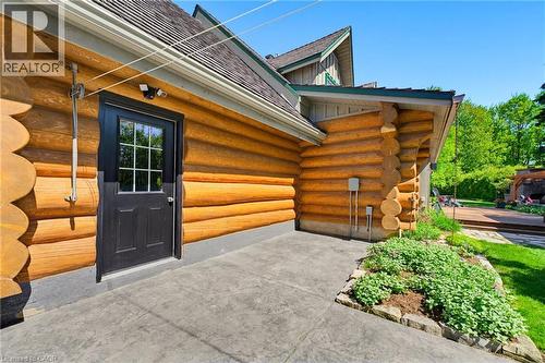Log cabin exterior featuring a black entry door with muntins, concrete patio, stone garden bed, and a partial wood deck - 169 James Street, Atwood, ON - Outdoor With Deck Patio Veranda With Exterior