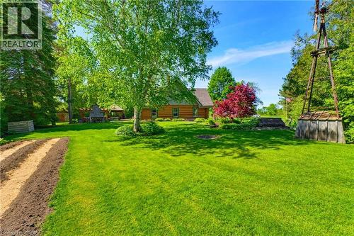 Expansive lawn with mature trees, a garden bed, a wooden gazebo with a built-in outdoor fireplace, and a log cabin style home - 169 James Street, Atwood, ON - Outdoor