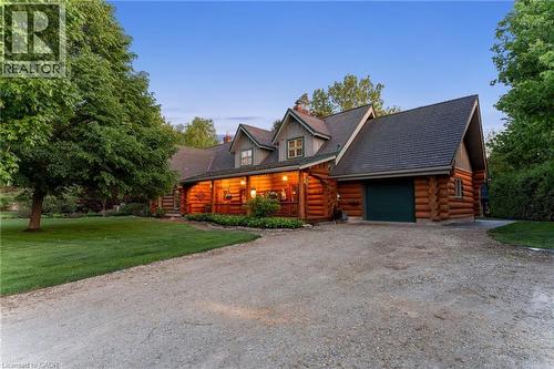 Log cabin architecture featuring a covered front porch, dormer windows, and an attached garage with a green door - 169 James Street, Atwood, ON - Outdoor