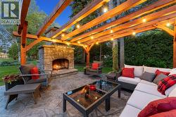 Outdoor entertaining space featuring a stone fireplace, stamped concrete patio, and a wood pergola with string lighting - 