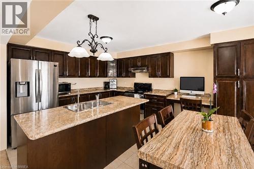 Kitchen featuring dark wood cabinetry, light beige countertops, stainless steel refrigerator, built-in desk area, and overhead lighting fixtures - 26 Pollard Street, Brantford, ON - Indoor