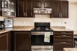 Modern kitchen featuring dark wood cabinetry, light-toned countertops, and a built-in stainless steel range with a coordinating range hood - 