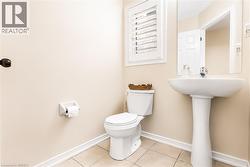 Pedestal sink with chrome faucet, ceramic toilet, window with white plantation shutters, wall-mounted mirror, and tile flooring - 
