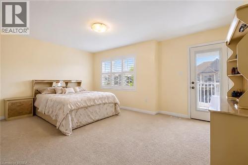 Carpeted bedroom featuring a large window with plantation shutters, a glass-paneled door opening to a white railing, a flush-mount ceiling light, and light-toned wall finishes - 26 Pollard Street, Brantford, ON - Indoor Photo Showing Bedroom