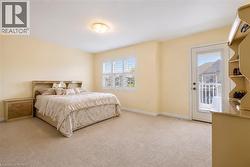 Carpeted bedroom featuring a large window with plantation shutters, a glass-paneled door opening to a white railing, a flush-mount ceiling light, and light-toned wall finishes - 