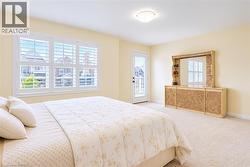 Bright room featuring a triple window with white plantation shutters, a glass-paneled exterior door leading to a balcony, and light-toned wall-to-wall carpeting - 